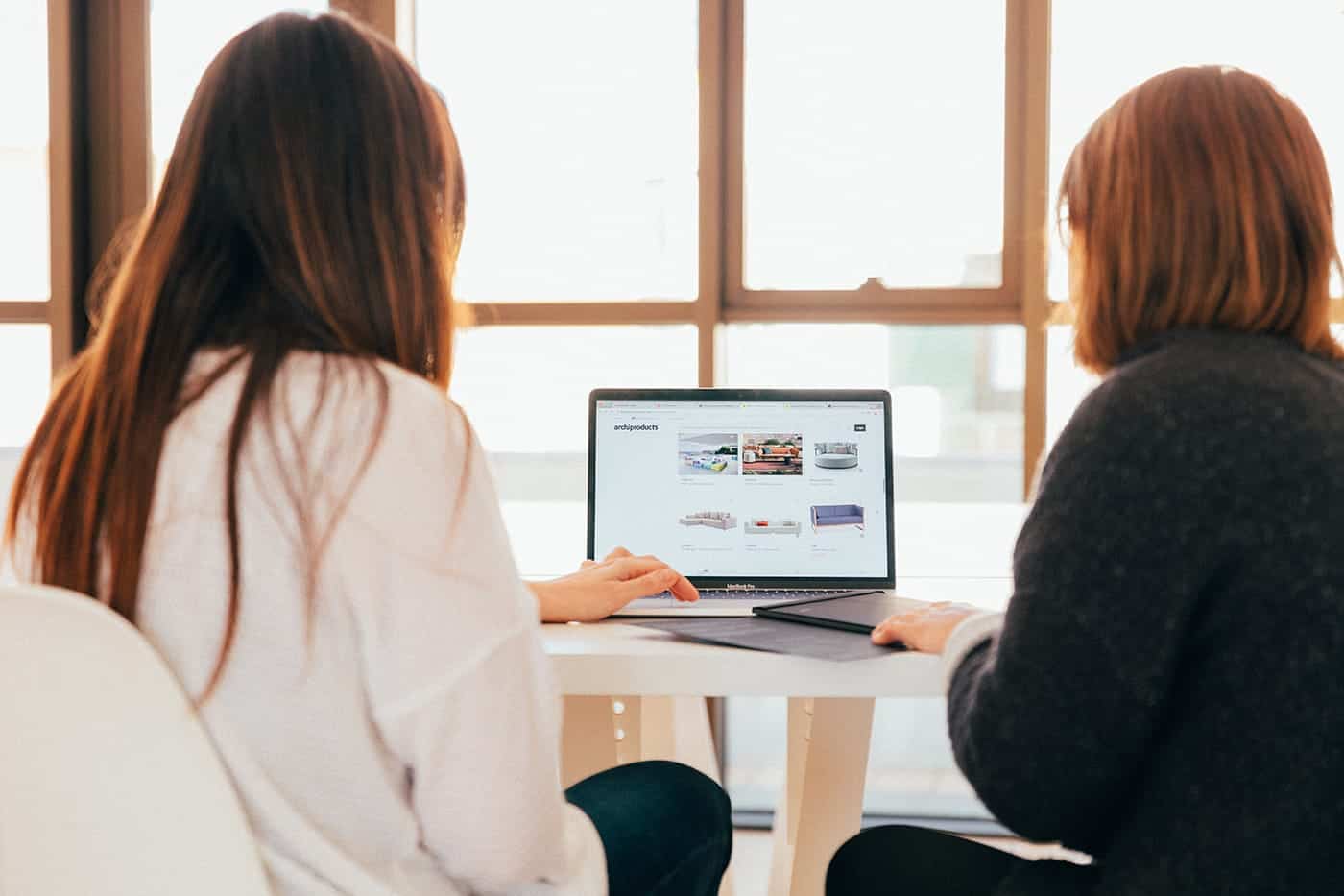a couple of women sitting at a table looking at a laptop