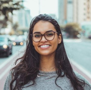 A young woman with glasses smiling on a city street, embracing urban lifestyle.