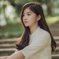 Asian woman in a white dress sitting on steps outdoors, showcasing elegance and beauty.